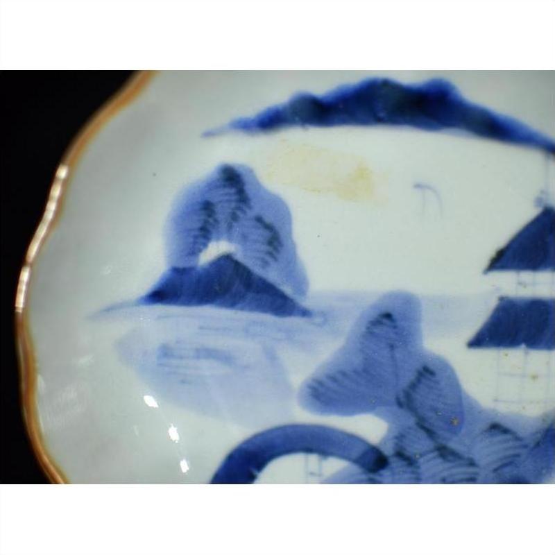 Close-up of antique Asian porcelain plate with hand painted misty peaks, arched bridge, and gold-trimmed edge.