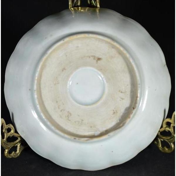 Close-up of the underside of a white porcelain plate with a round foot ring on a gold stand.