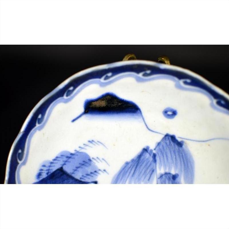 Close-up of blue and white hand painted porcelain plate with river pavilion and willow grove, wavy patterned border.