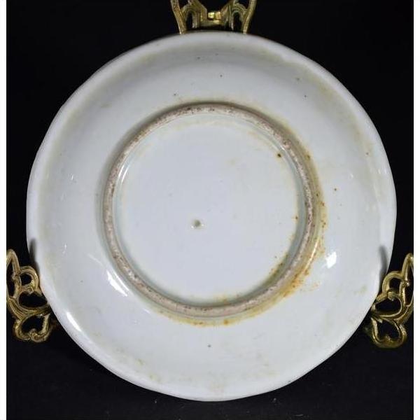 Close-up of an antique hand painted porcelain plate with visible wear on underside, displayed on a gold stand.