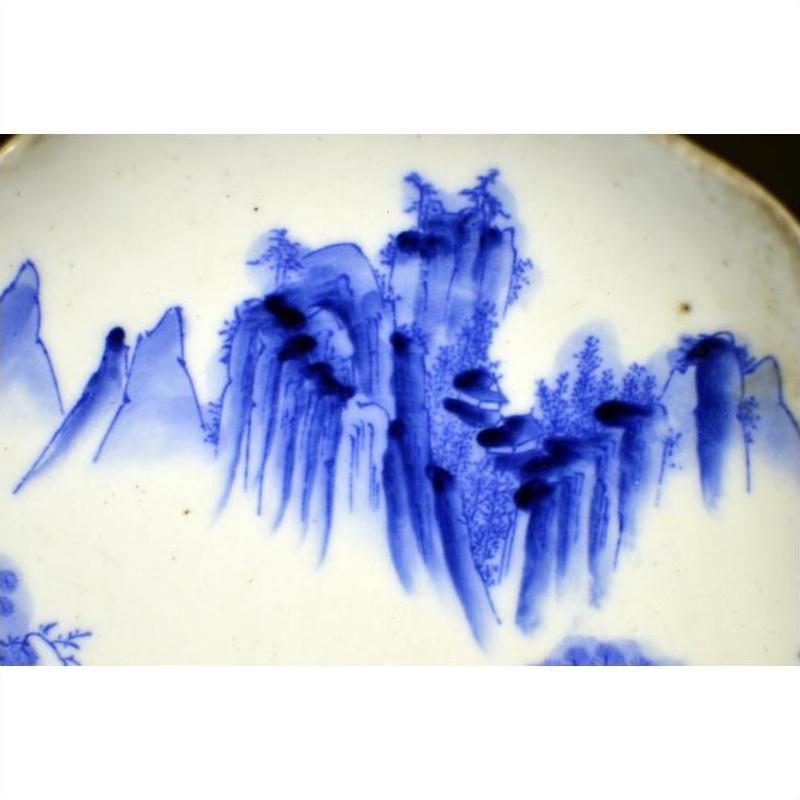 White porcelain plate with hand-painted mountain landscape and willow trees in traditional Asian style, close-up view.