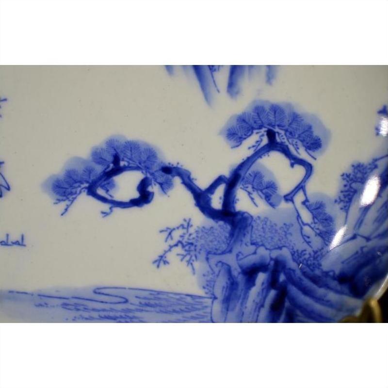 Close-up of blue and white hand painted porcelain plate with mountain landscape and willow trees detailing.