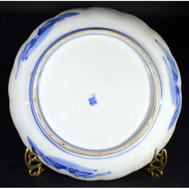 Close-up of the underside of a white porcelain plate with blue mountain landscape, blue stamp, on brass stand.
