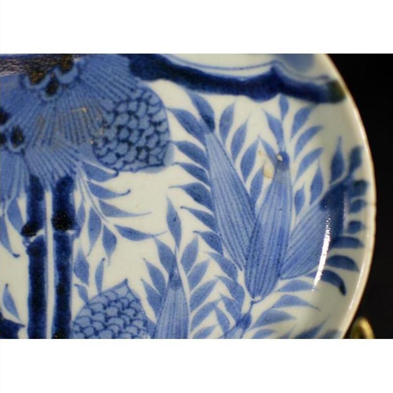 Close-up of antique Asian porcelain plate with hand painted pine cone cluster and dense green foliage details.