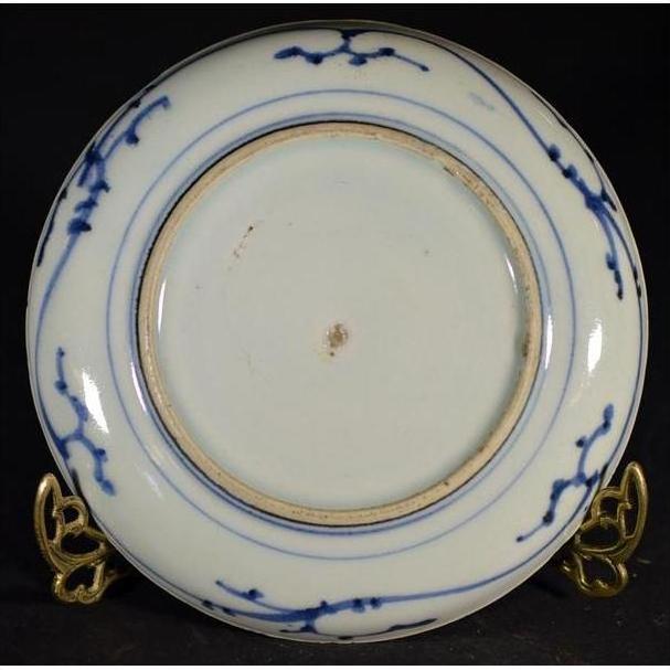 Close-up of underside of white porcelain plate with hand painted pine cone cluster and dense foliage, on brass stand.
