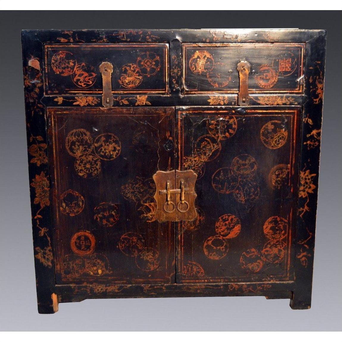 Black lacquer Chinese wood cabinet with gold details, red floral motifs, two drawers, and scalloped metal hardware.