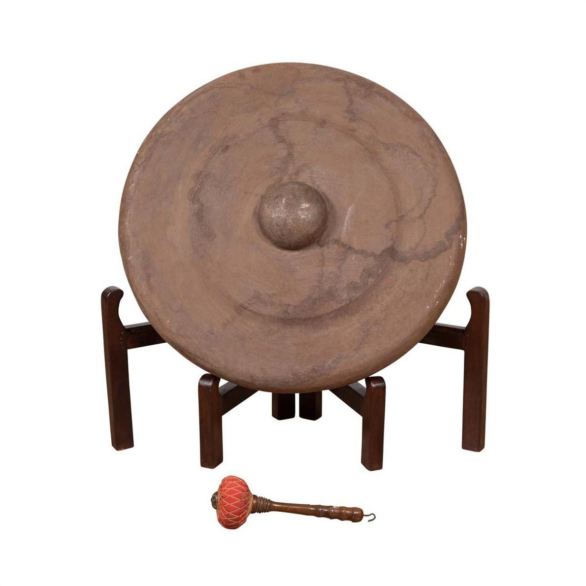 Bronze Burmese temple gong with raised center on stand, red mallet in front, close-up view.