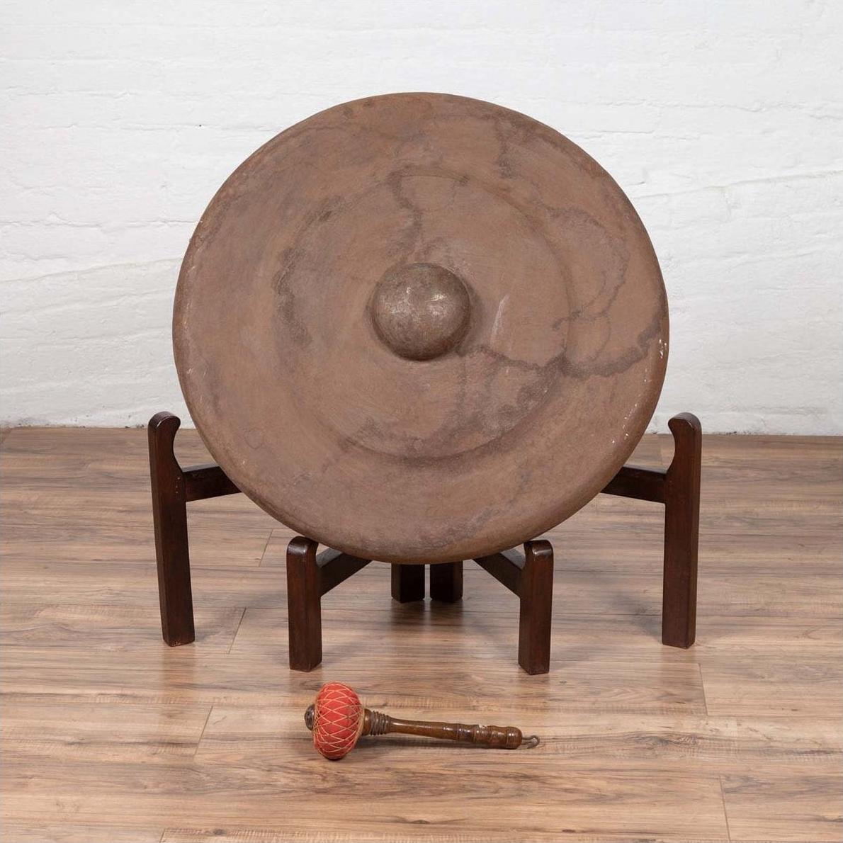 Bronze Burmese temple gong with raised center, red mallet, on wooden stand, close-up.