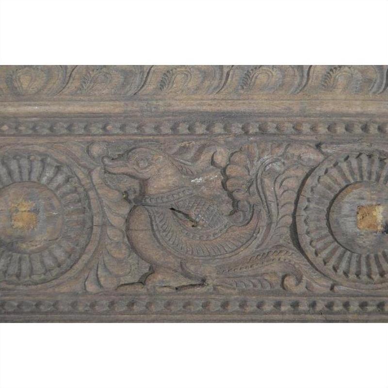 Close-up of antique wooden Indian carving with stylized mythical animal and swirling circular floral patterns.