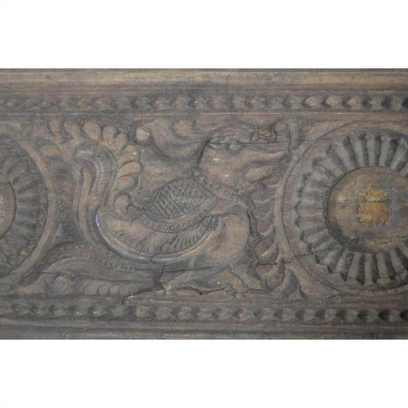 Brown wooden Indian carving of a stylized bird with intricate circular and floral patterns, close-up view.