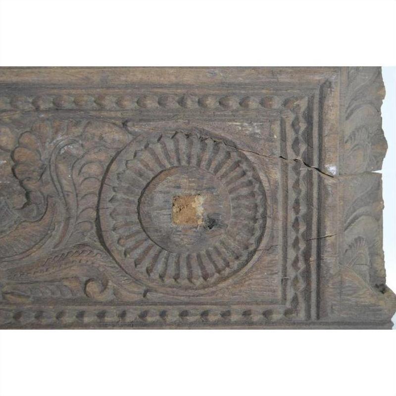 Brown carved wood panel with floral, geometric, and circular designs; visible cracks and rich patina, close-up view.