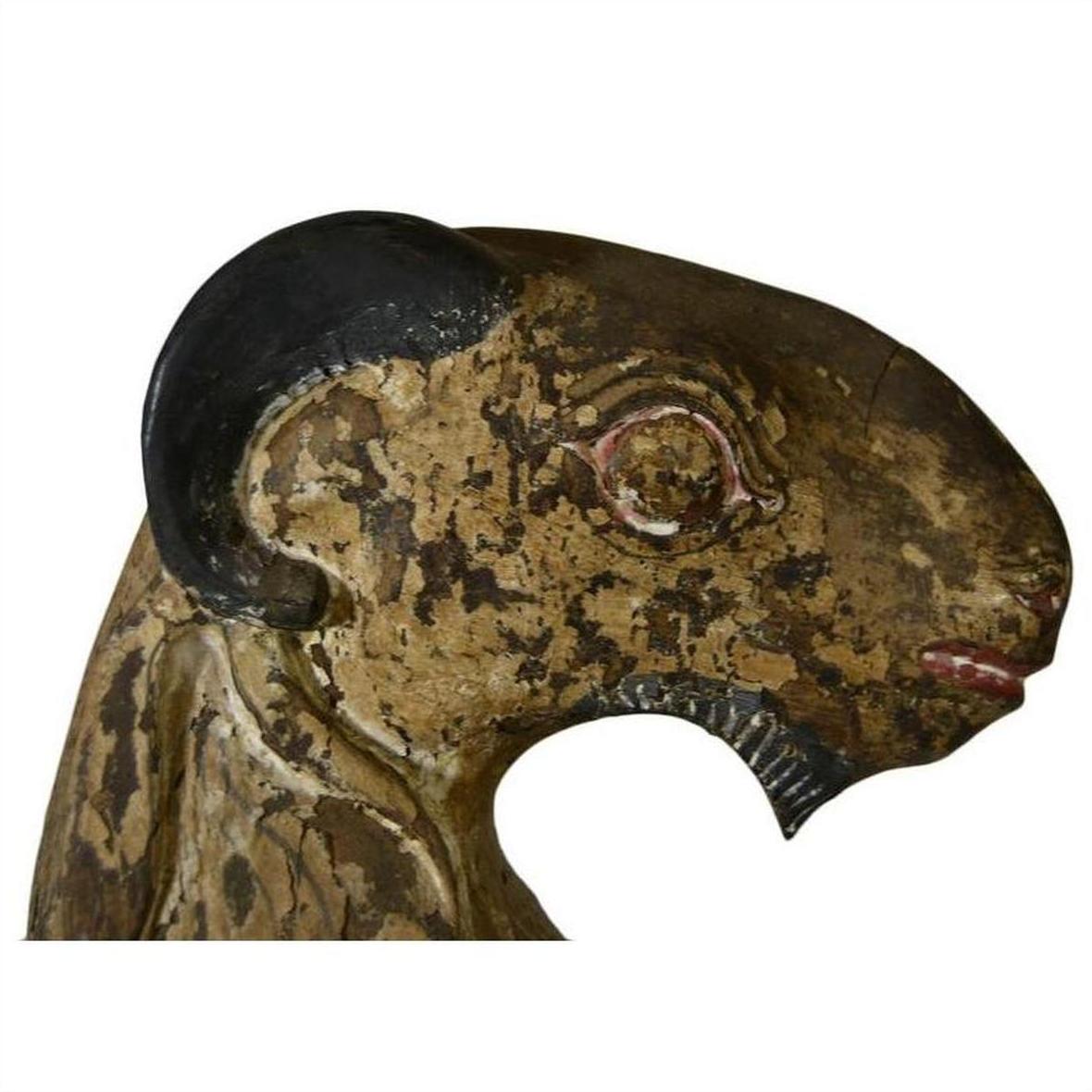 Brown hand-carved wood goat sculpture with black horn, painted and weathered details, seated position.