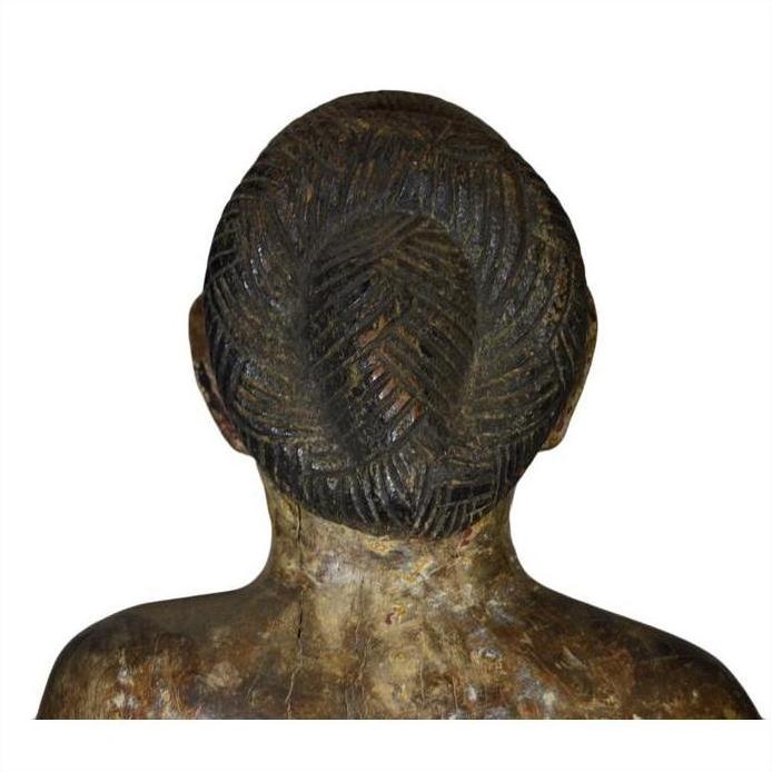 Brown wooden carving, back view, showing intricately braided hair and textured head and shoulders.