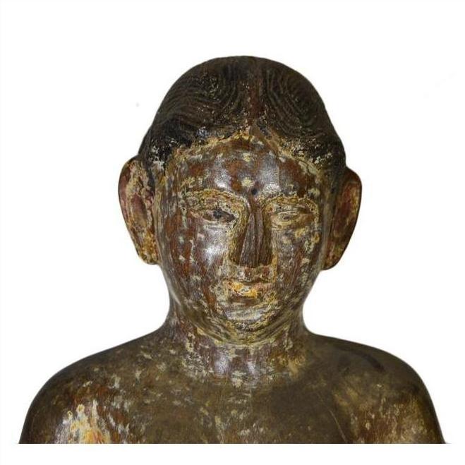 Close-up of an antique wooden Burmese temple carving, showing a serene, large-eared human figure.