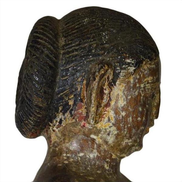 Brown aged wooden sculpture of woman with bun, side view, weathered texture, antique Burmese temple carving.
