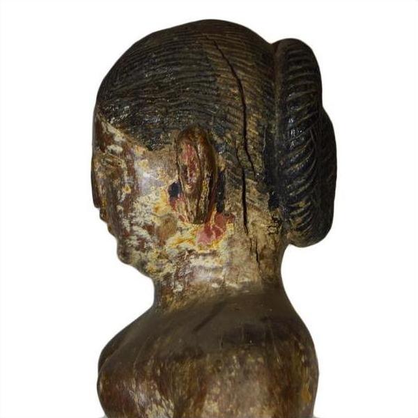 Weathered wooden statue of a woman with hair in a bun, side view.
