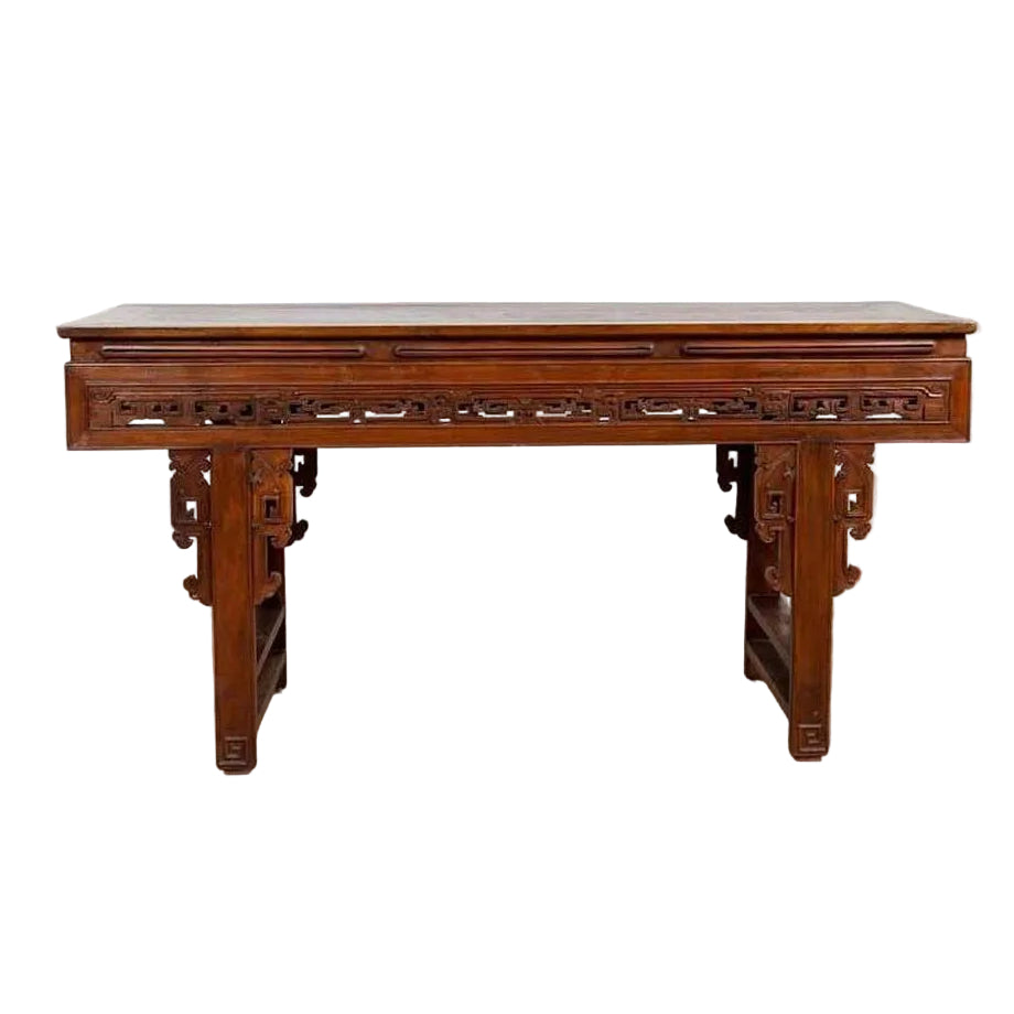 Dark wood Chinese altar console with overhang top and open fretwork scrolls, placed by a white brick wall on wooden floor.