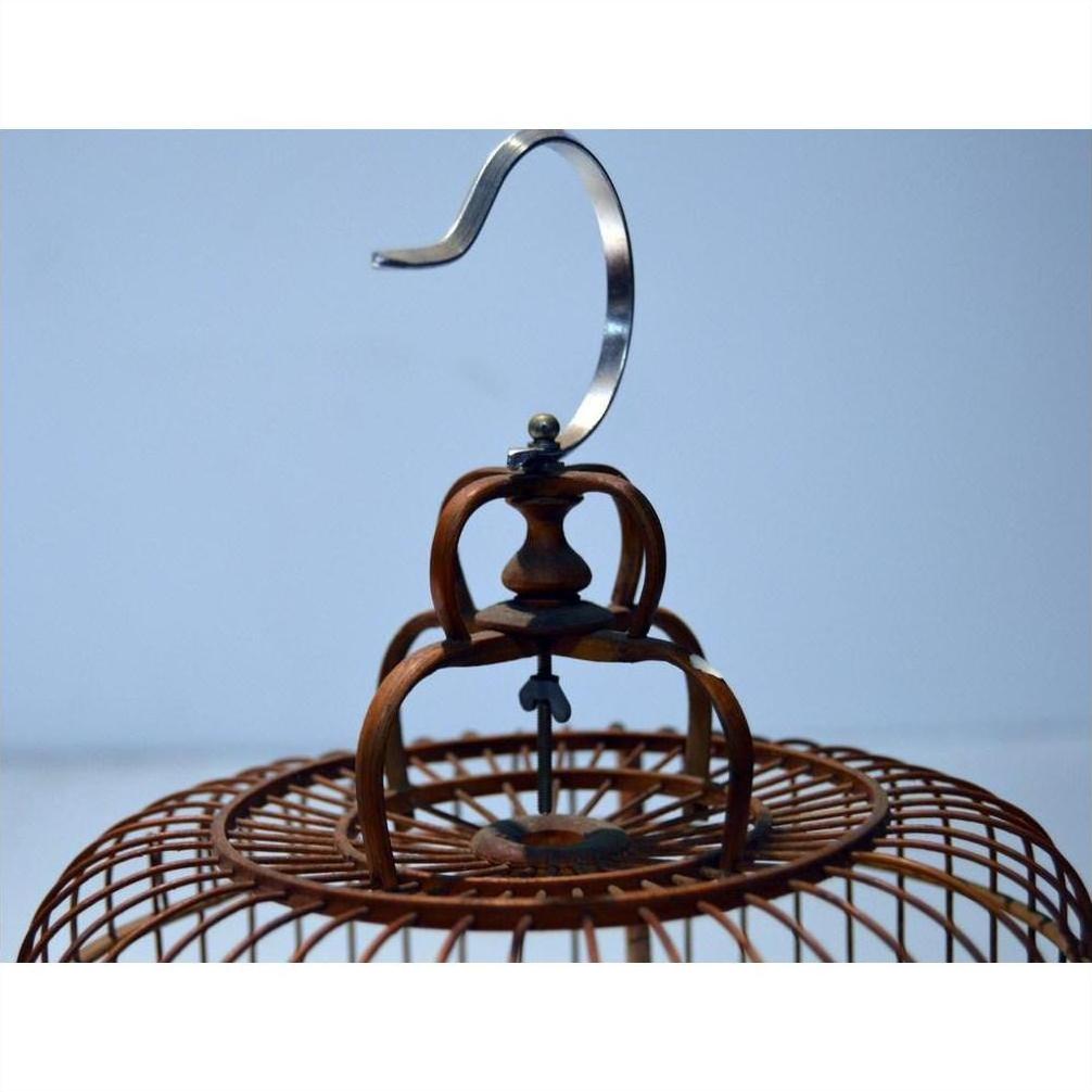 Close-up of brown antique Chinese bird cage top with silver hook on light blue background.