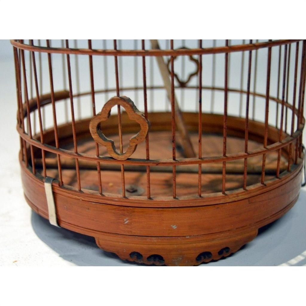 Close-up of an antique Chinese bird cage with vertical metal bars and quatrefoil accent, warm brown finish.