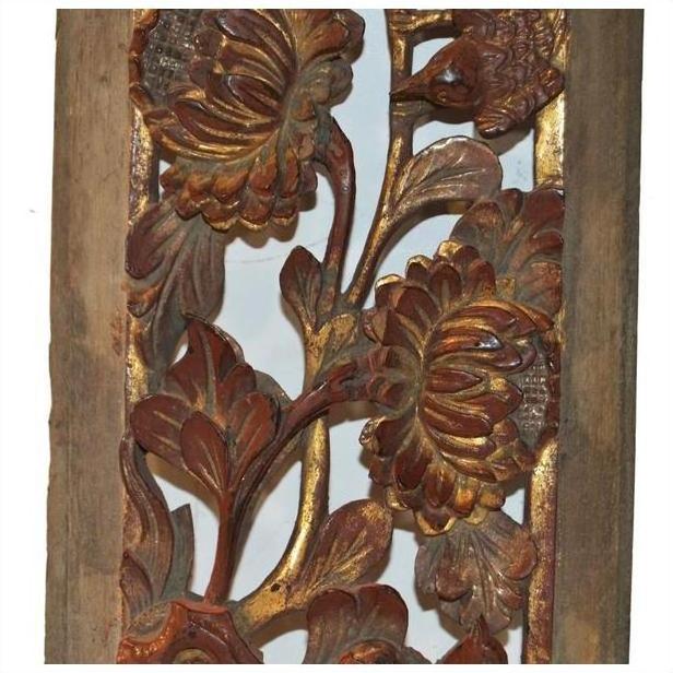 Close-up of an antique carved wooden panel with gold and red floral designs and a bird among ornate leaves.