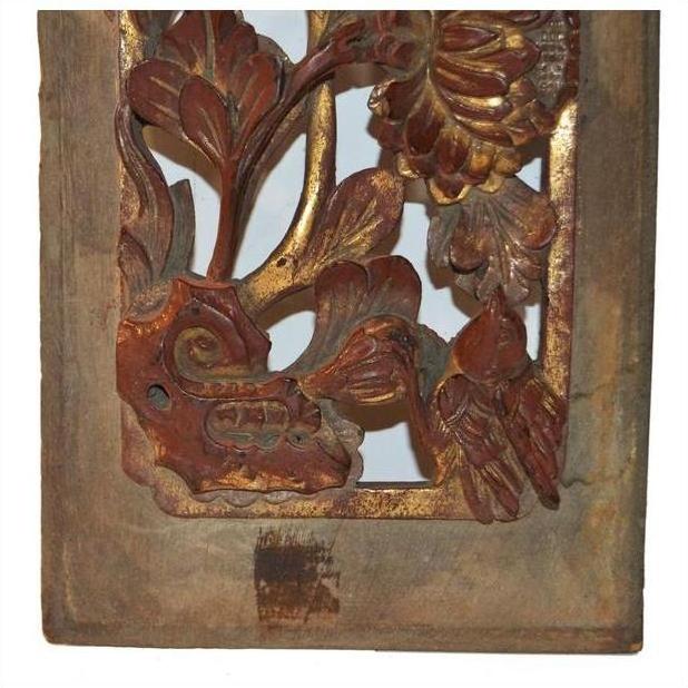 Close-up of a brown wooden panel with floral carvings and gold accents in a rectangular frame.
