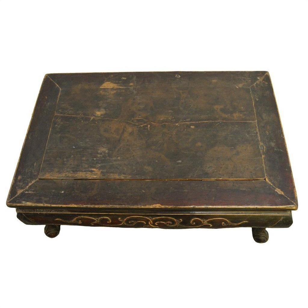 Rectangular antique Indonesian wood table with ornate gold carvings and four short hand-carved legs, close-up view.