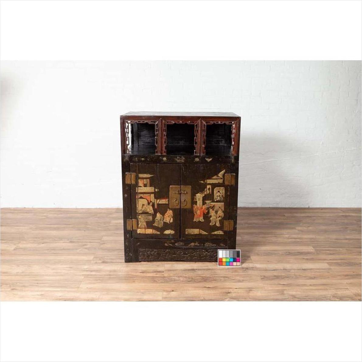 Black lacquered wood Chinese display cabinet with hand painted chinoiserie and open shelf, against white brick wall.