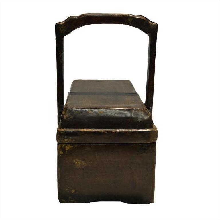 Brown wooden antique Chinese dowry box with tall rectangular handle and hinged lid, close-up.