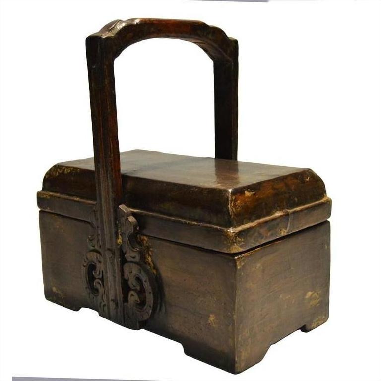 Dark wood Chinese dowry box with ornate carvings and metal handle, close-up on polished finish.