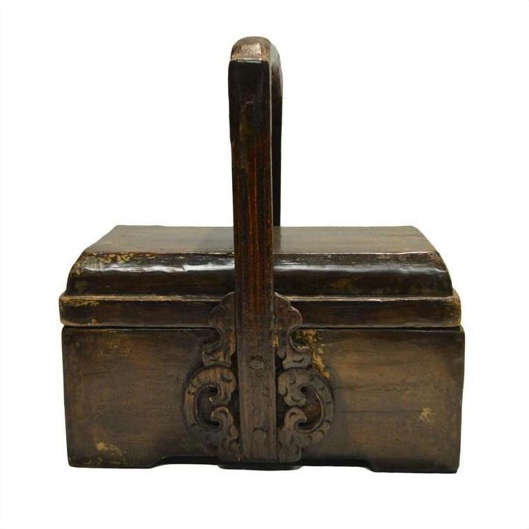 Brown wooden Chinese dowry box with curved handle and ornate carved metal accents on the front, close-up view.
