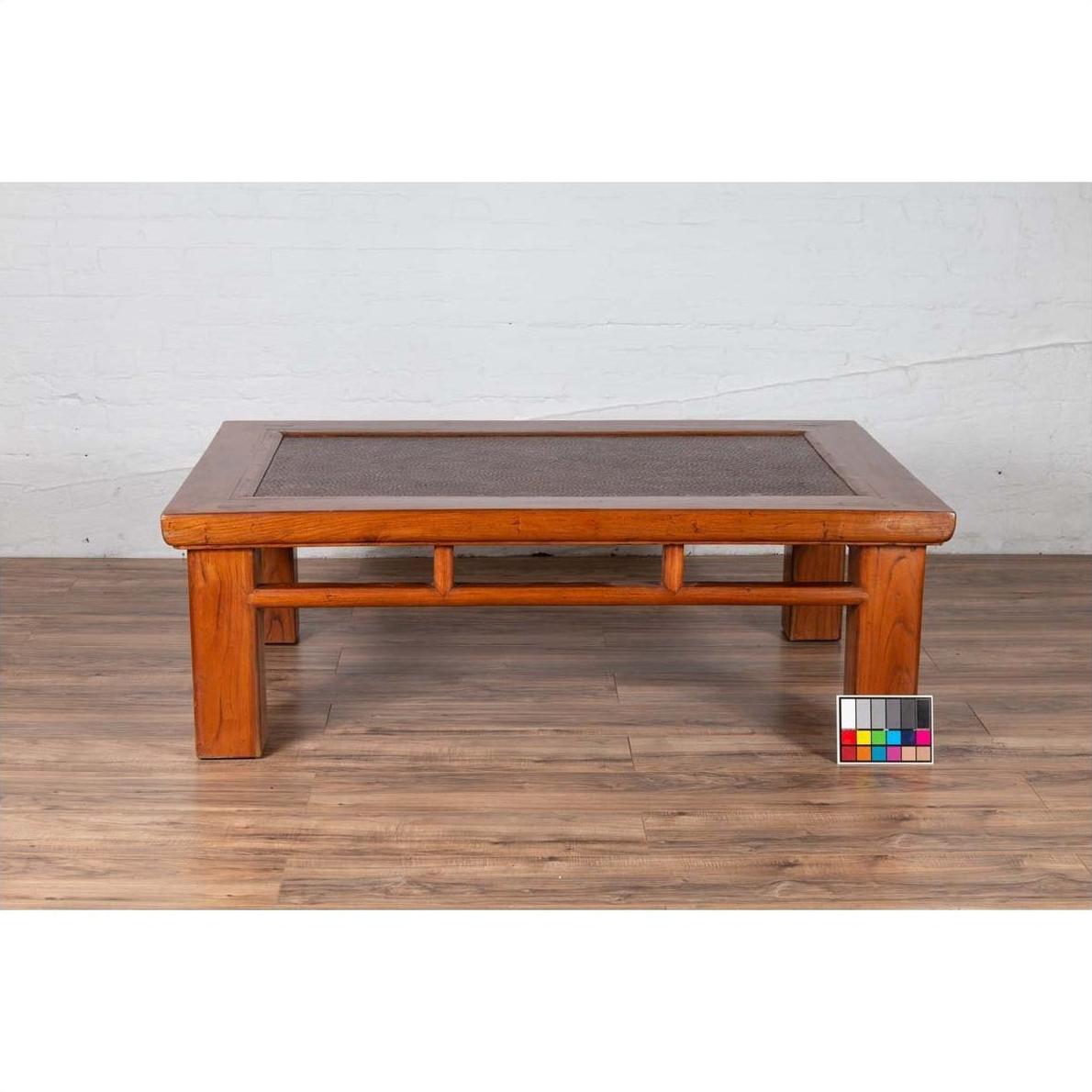 Brown Chinese Elm coffee table with square legs and rattan inset top, on wood floor with color card nearby.
