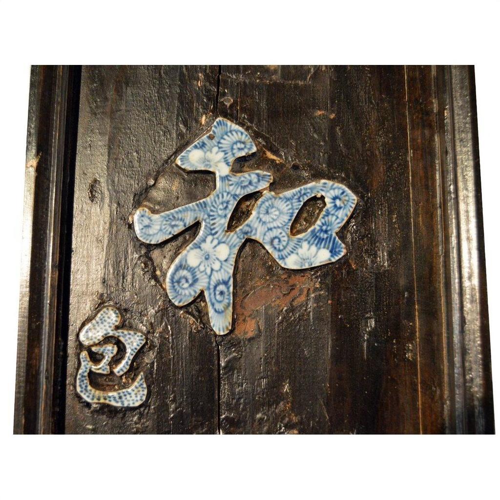 Close-up of antique Chinese enamel calligraphy sign with blue and white characters on dark weathered wood.