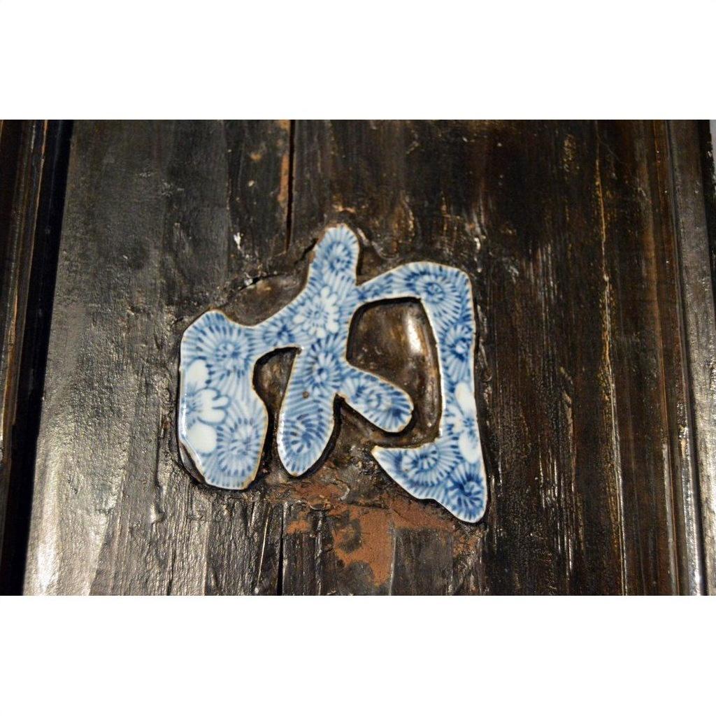 Blue and white enamel floral porcelain calligraphy sign on dark distressed wood, close-up view.