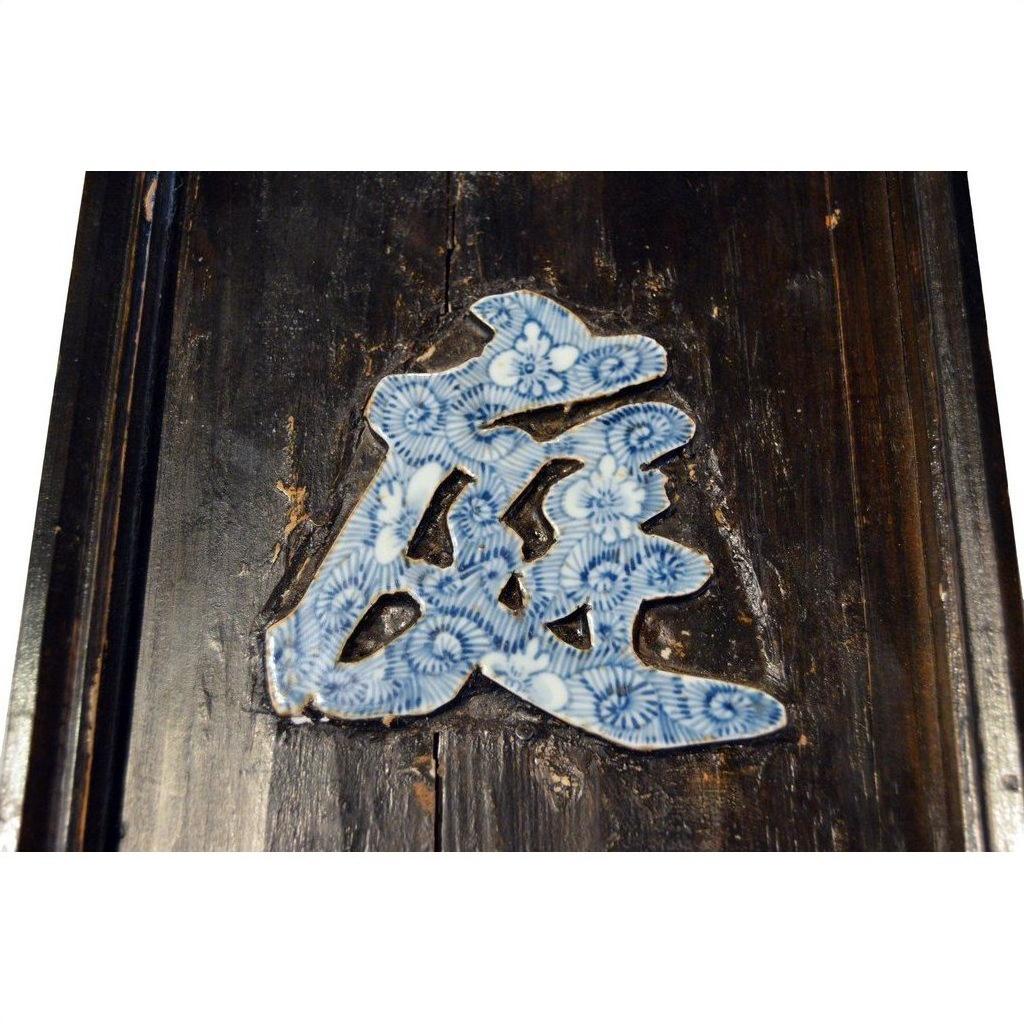 Close-up of blue floral patterns on antique Chinese enamel calligraphy sign, displayed on a dark wooden plaque.