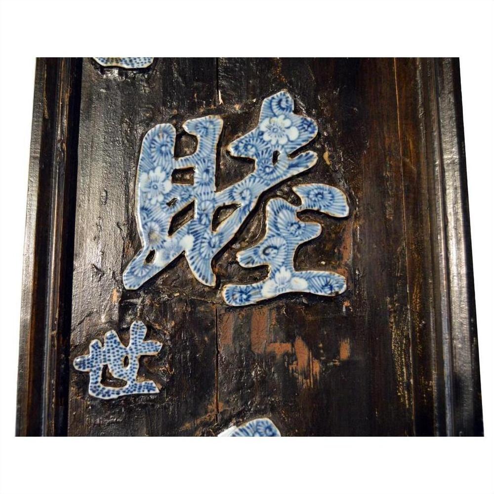Blue and white enamel Chinese calligraphy sign with ornate relief, set on detailed dark wood background, close-up view.