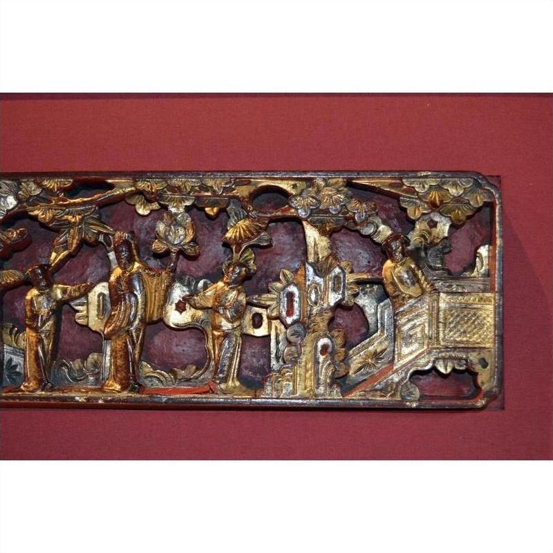 Gold gilt wood carving with ornate Chinese figures, trees, and architectural details in a garden scene, close-up view.