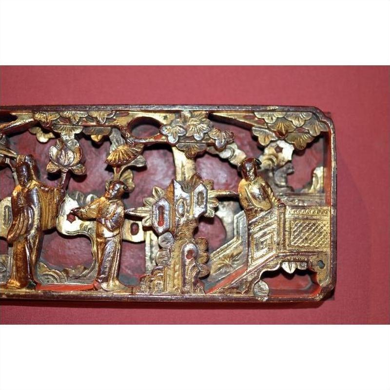 Close-up of gold and red hand-carved wood Chinese antique carving with three figures on temple wall.