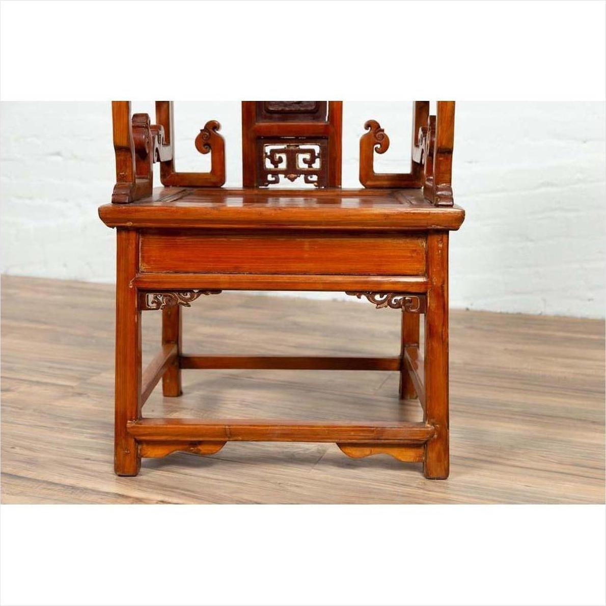 Natural wood antique hand-carved Chinese chair on wooden floor against white brick wall indoors.