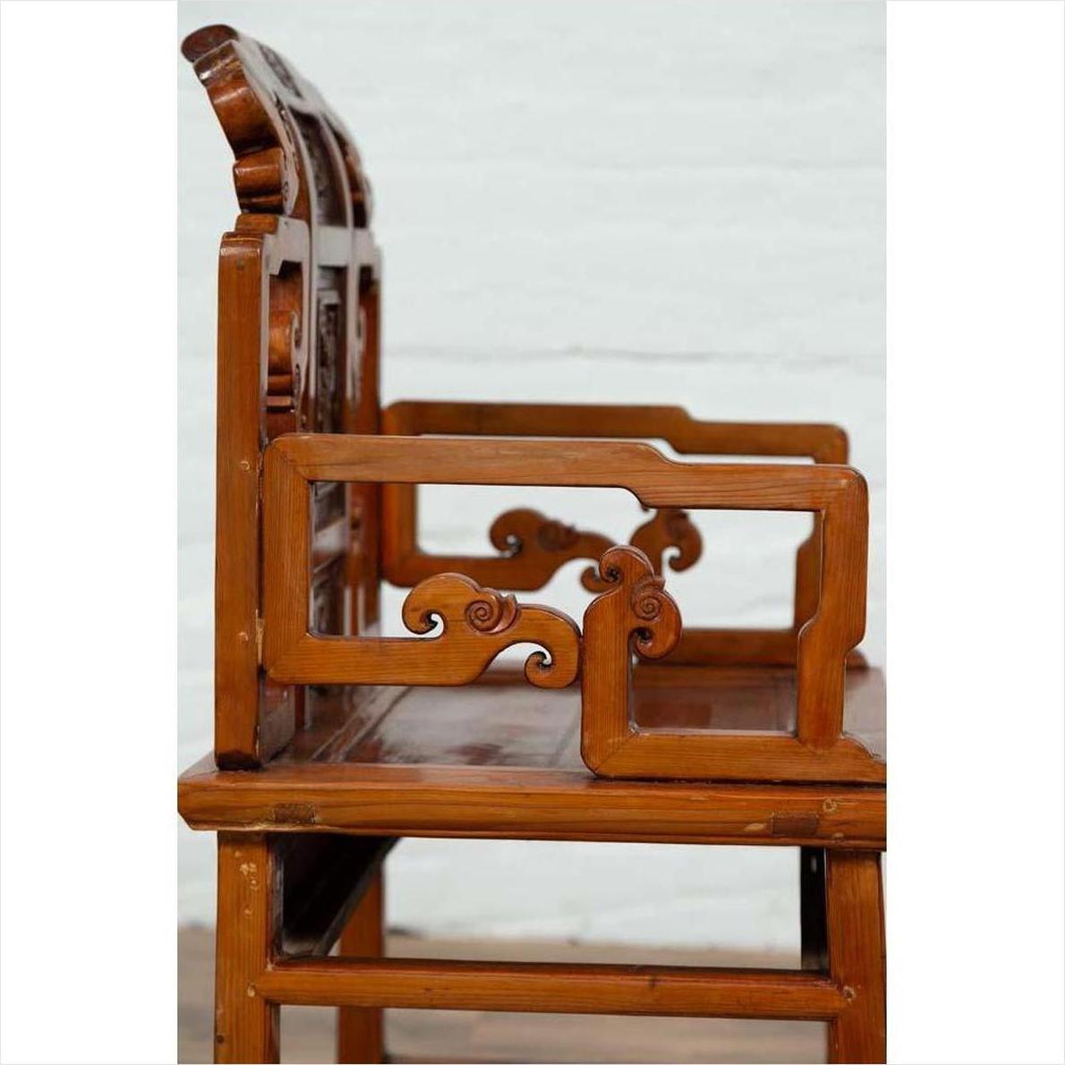 Brown wood chair with ornate hand-carved scrollwork, side view, showing natural wood patina.