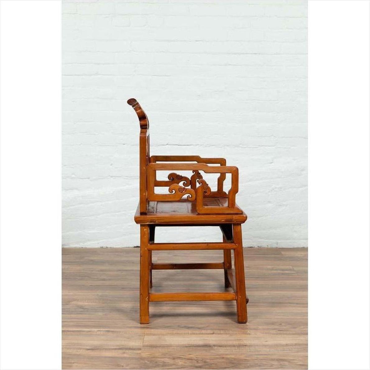 Brown wood hand-carved chair with natural patina on wooden floor against white brick wall indoors.
