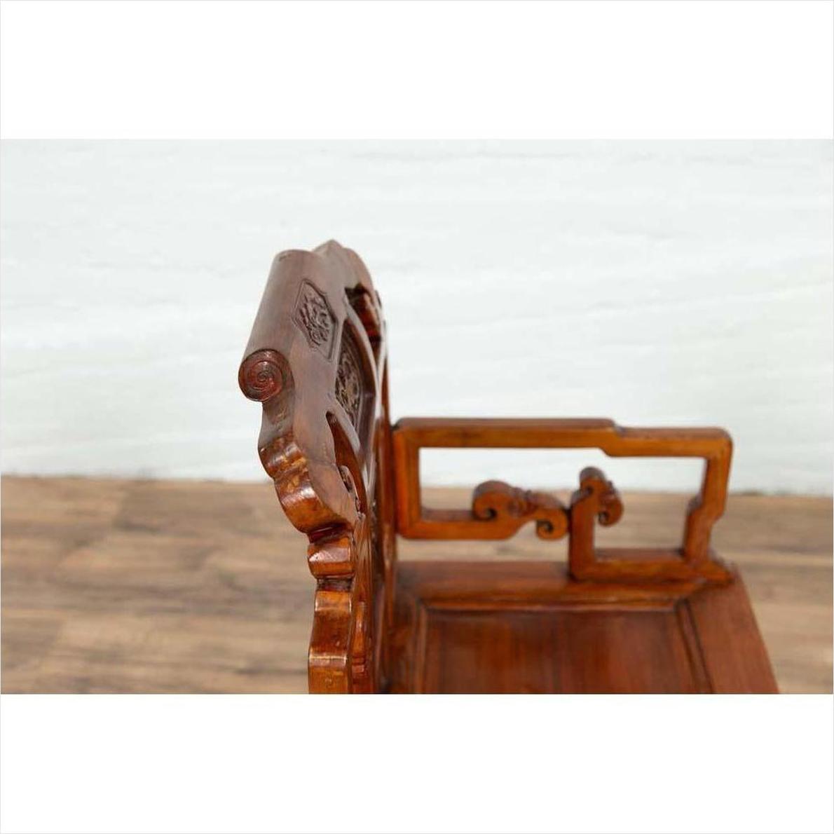 Close-up of natural wood antique Chinese chair with hand-carved details on backrest and armrest.