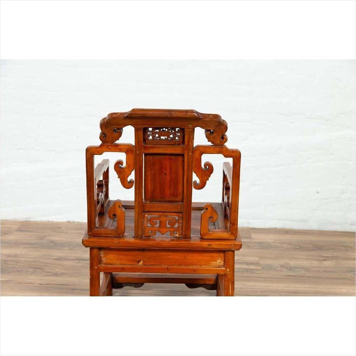 Brown wood hand-carved chair with natural patina, back view, against white wall and wood floor indoors.