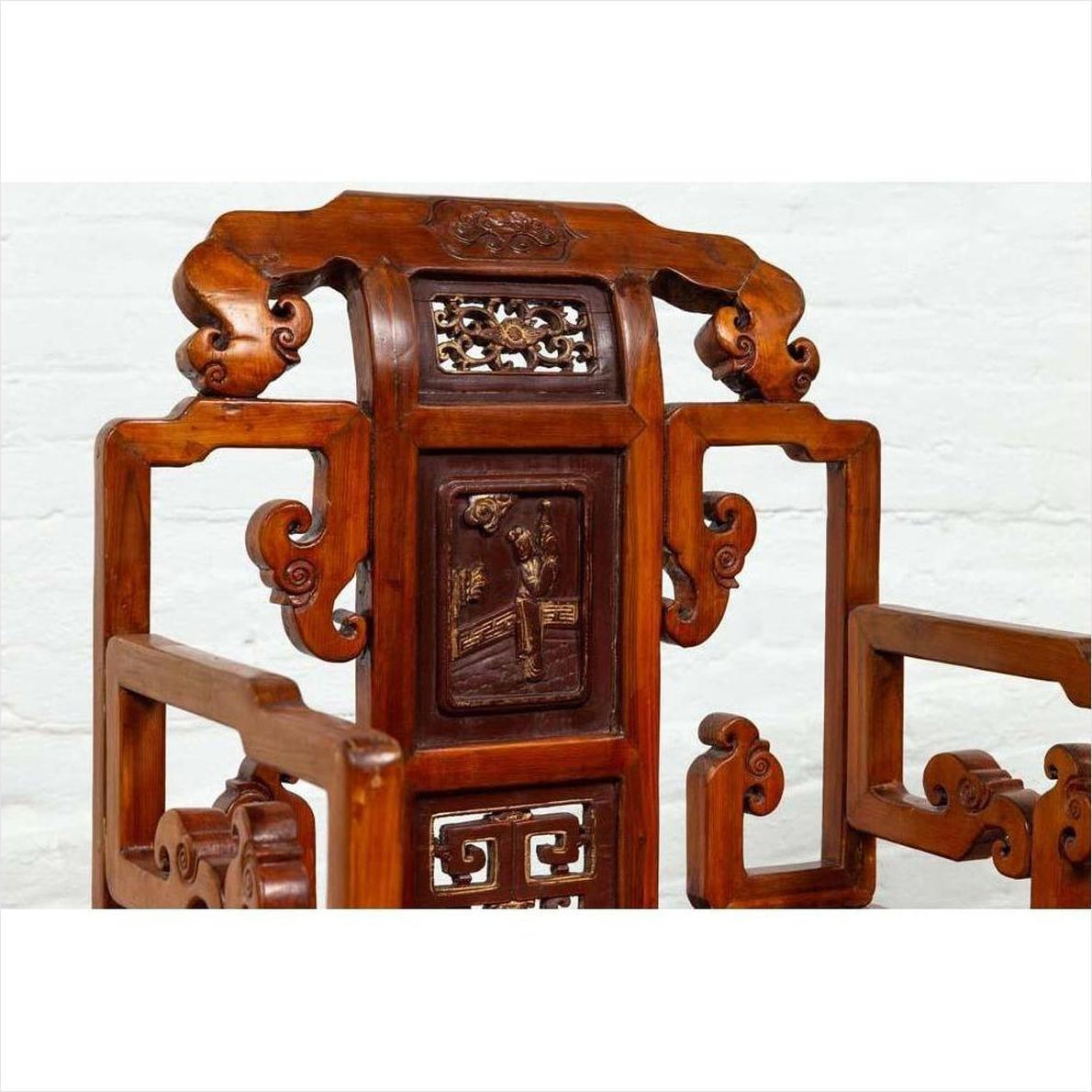 Brown wood hand-carved Chinese chair with geometric armrests and natural patina, set indoors against a white brick wall.