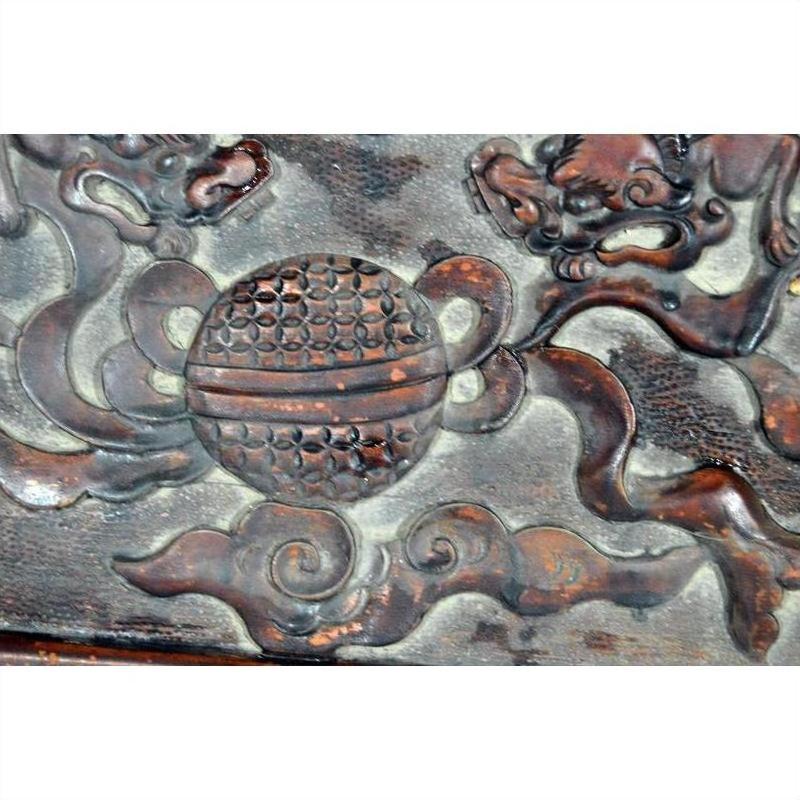 Close-up of antique Chinese red lacquered rosewood plaque with hand-carved ball, clouds, and mythical creature motifs.