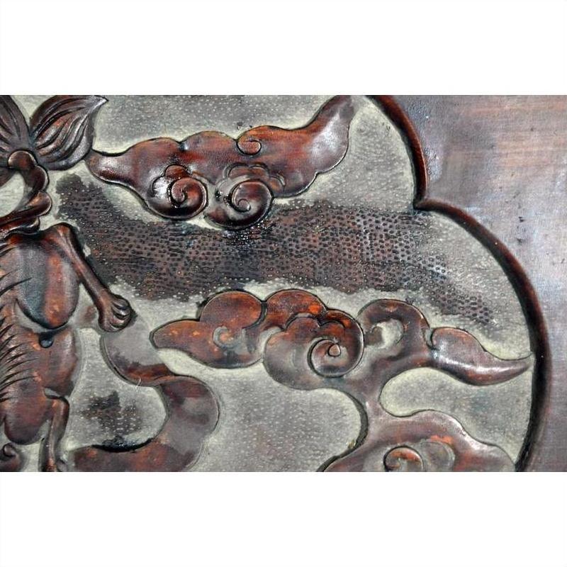 Close-up of red lacquered rosewood wall plaque with hand-carved swirling cloud designs.