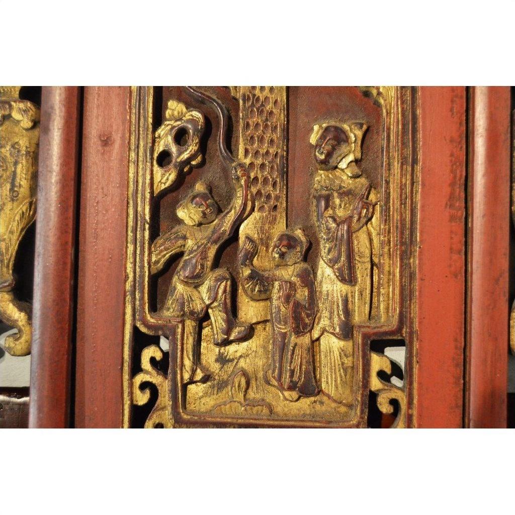 Red lacquer and gilt wood Chinese panel with three figures in traditional dress, textured background, close-up view.