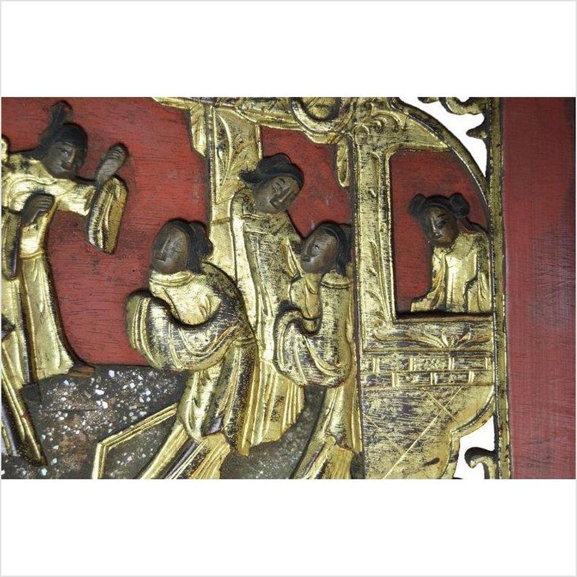 Red wooden panel with gold-painted hand-carved traditional Chinese figures engaged in daily activities.