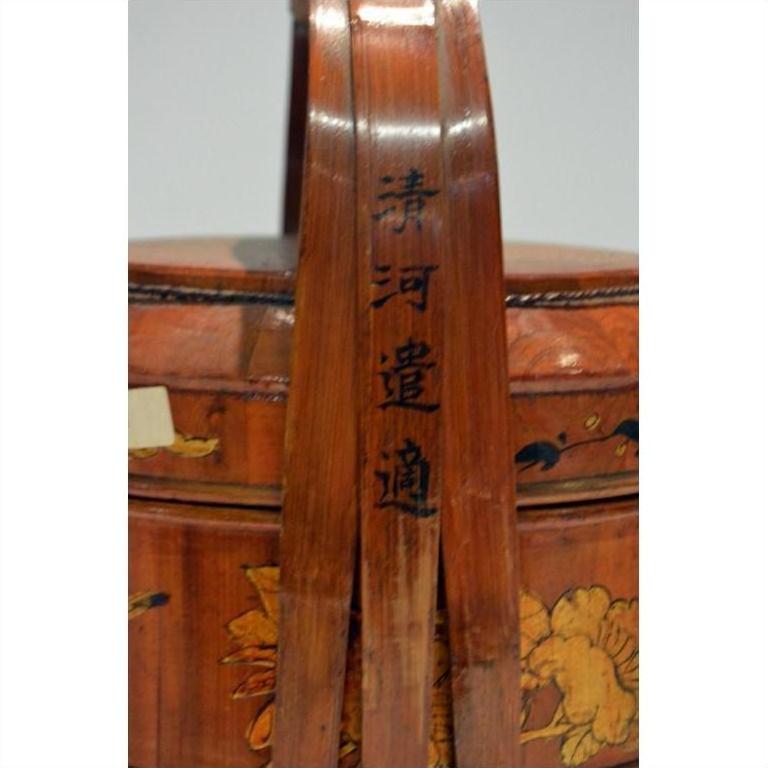 Close-up of a bamboo basket handle, hand painted with black Chinese characters and floral designs.