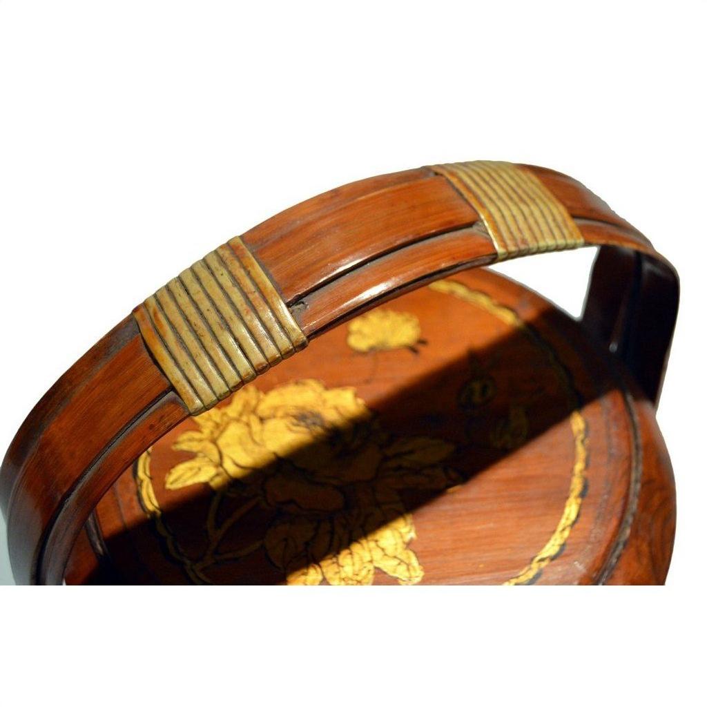 Close-up of a brown bamboo basket with hand painted floral design and gold bands on handle, seen indoors.