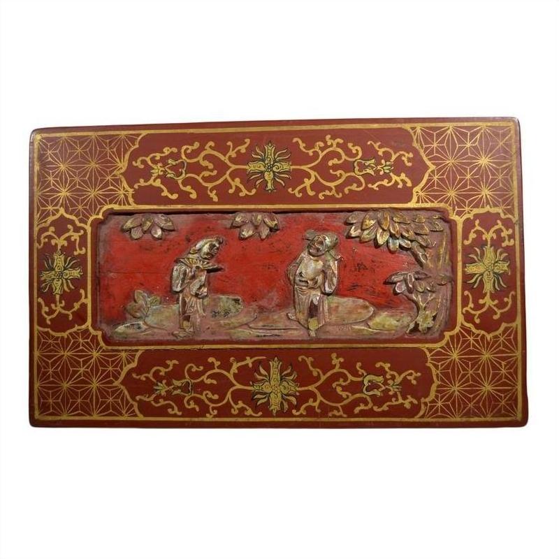 Red and gold Chinese lacquer box with floral inlay and raised scene of two figures under trees, close-up view.